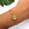 Detalhe do pulso feminino usando a Pulseira Mini Asas em aço dourado da Swaminah. Design delicado e alado para aromaterapia pessoal, destacando o brilho do ouro na pele.