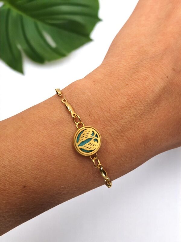 Detalhe do pulso feminino usando a Pulseira Mini Asas em aço dourado da Swaminah. Design delicado e alado para aromaterapia pessoal, destacando o brilho do ouro na pele.