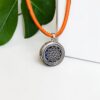 Pulseira Vahani Mandala em prata com fundo de cortiça laranja. Detalhe da geometria sagrada da mandala em metal sobre textura natural de cortiça para aromaterapia Swaminah.