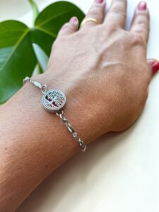 Detalhe de mão feminina usando a Pulseira Mini Árvore da Vida em prata da Swaminah. Design delicado para aromaterapia pessoal com foco no pingente vazado